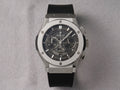 Hublot Big Bang chronograph watch with a black dial and black rubber strap, set in a silver-toned titanium case on a textured gray background.