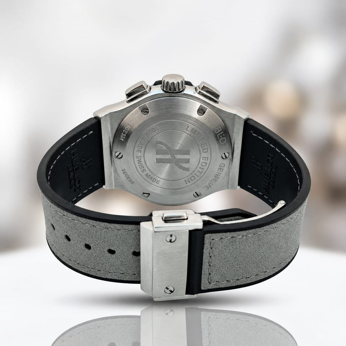 Back view of a Johnnie Walker Limited Edition watch with a silver-tone stainless steel case and a gray textured strap with black edges, on a reflective white surface.